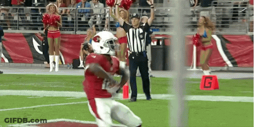 A Football Player Is Running On The Field With Cheerleaders And A Referee GIF