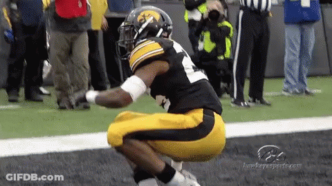 A Football Player Is Squatting Down On The Field While A Referee Looks On GIF