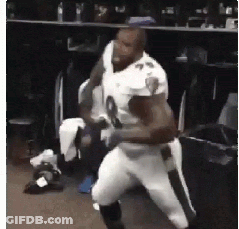 A Football Player Is Standing In A Locker Room With Another Player . GIF
