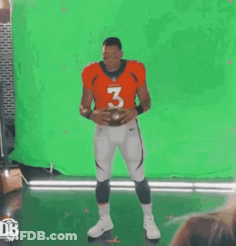 A Football Player Is Standing In Front Of A Green Screen And Holding A Football . GIF