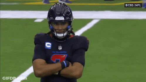 A Football Player Is Standing On A Field With His Arms Crossed And A Referee Standing Behind Him . GIF