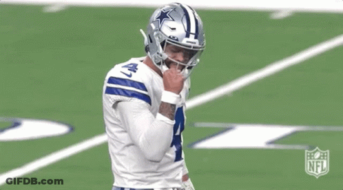 A Football Player Is Standing On A Field With His Hand On His Face . GIF