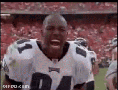 A Football Player Is Standing On A Field With His Mouth Open And A Crowd Behind Him . GIF