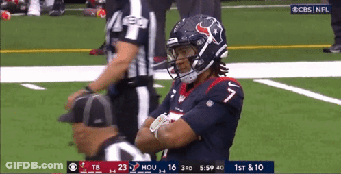 A Football Player Is Standing On The Field With His Arms Crossed And A Referee Standing Behind Him . GIF