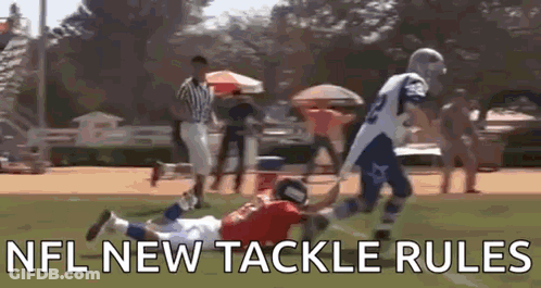 A Football Player Is Trying To Tackle Another Player On A Field While A Referee Watches . GIF