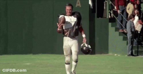 A Football Player Is Walking On The Field Holding A Helmet And A Football . GIF