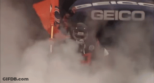 A Football Player Is Walking Through A Cloud Of Smoke While Wearing A Helmet . GIF
