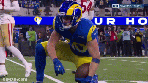 A Football Player Kneeling On The Field With A Fox Championship Logo Behind Him GIF