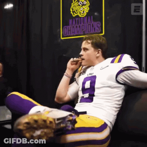 A Football Player Sitting On A Couch With A National Champions Sign Behind Him GIF
