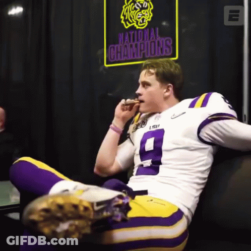A Football Player Sitting On A Couch With A Sign That Says National Champions Behind Him GIF