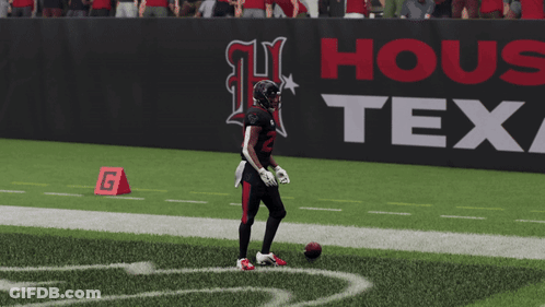 A Football Player Stands On The Field In Front Of A Sign That Says Texas GIF