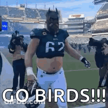 A Football Player Wearing A Batman Mask And A Helmet Is Walking On A Field . GIF