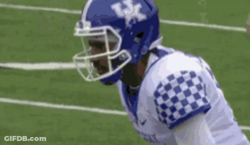 A Football Player Wearing A Blue Helmet And A Checkered Jersey Is Standing On The Field . GIF