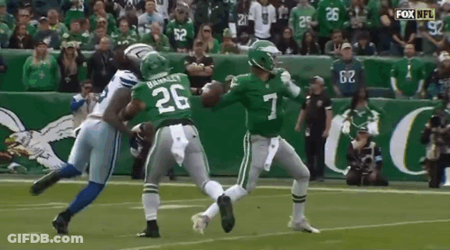 A Football Player Wearing A Green Jersey With The Number 7 On It Is Being Tackled By Another Player . GIF