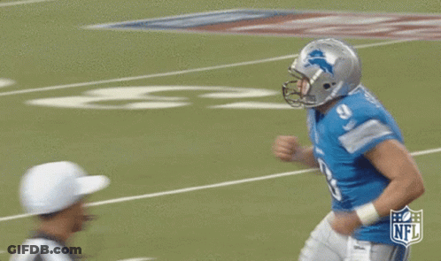 A Football Player Wearing A Helmet And A Blue Shirt Is Running On A Field . GIF