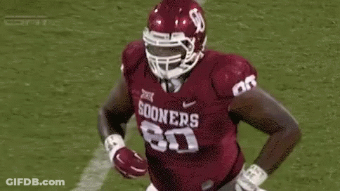 A Football Player Wearing A Helmet And A Maroon Jersey Is Running On The Field . GIF
