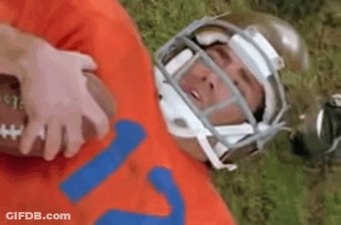 A Football Player Wearing A Helmet Is Laying On The Grass With A Football . GIF