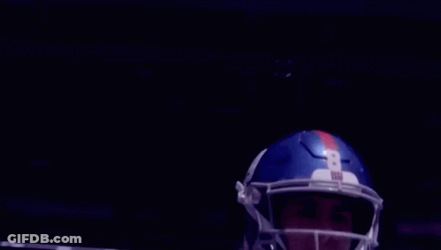 A Football Player Wearing A Helmet Is Standing In Front Of A Stadium . GIF