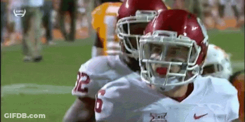 A Football Player Wearing A Helmet Is Standing Next To Another Player On The Field . GIF