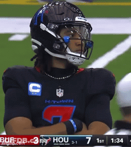 A Football Player Wearing A Helmet Stands On A Field With His Arms Crossed GIF