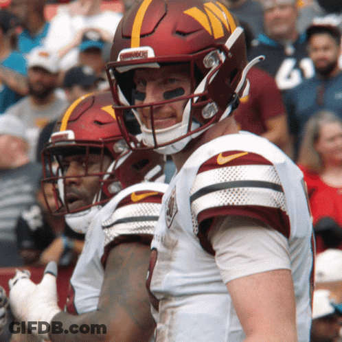 A Football Player Wearing A Helmet That Says Washington Stands Next To Another Player GIF