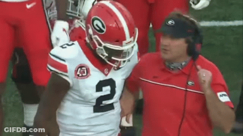 A Football Player Wearing A Helmet With The Number 2 On It Is Running On The Field While A Coach Watches . GIF