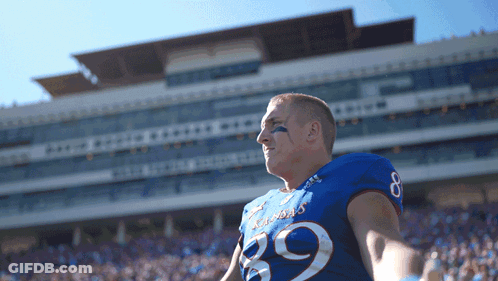 A Football Player Wearing A Kansas Jersey Stands In Front Of A Stadium GIF
