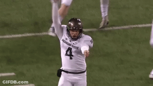 A Football Player Wearing A Michigan State Jersey Is Kicking A Ball On The Field . GIF