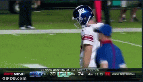 A Football Player Wearing A Ny Giants Helmet Talks To A Referee On The Field GIF