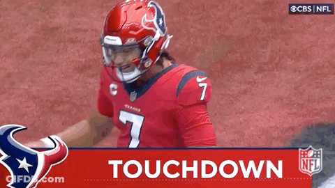 A Football Player Wearing A Red Helmet Is Standing On A Field With The Words `` Touchdown '' Behind Him . GIF