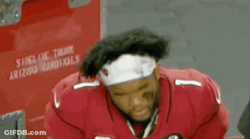 A Football Player Wearing A Red Jersey And A White Headband Is Sitting In A Locker Room . GIF