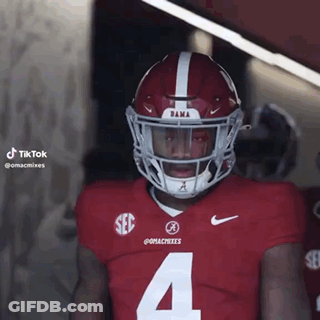 A Football Player Wearing A Red Jersey And A White Helmet Is Standing In A Locker Room . GIF