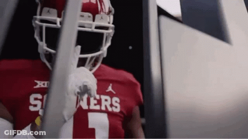 A Football Player Wearing A Red Jersey And White Helmet Is Standing In A Locker Room . GIF