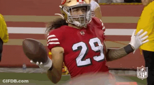 A Football Player Wearing A Red Jersey With The Number 29 On It Is Holding A Football In His Hand . GIF