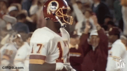 A Football Player Wearing A Redskins Uniform And Helmet Is Standing In Front Of A Crowd . GIF