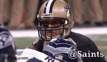 A Football Player Wearing A Saints Helmet Looks At Another Player GIF