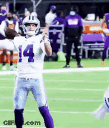 A Football Player Wearing A White And Purple Uniform Is Standing On A Field . GIF
