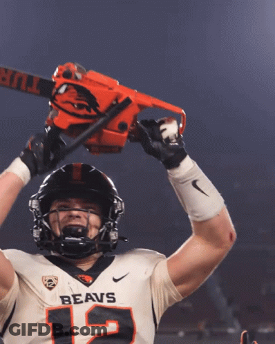 A Football Player With The Number 12 On His Jersey Is Holding A Chainsaw Over His Head GIF