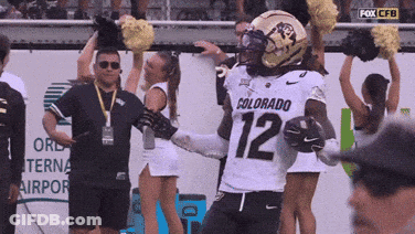 A Football Player With The Number 12 On His Jersey Stands In Front Of Cheerleaders GIF
