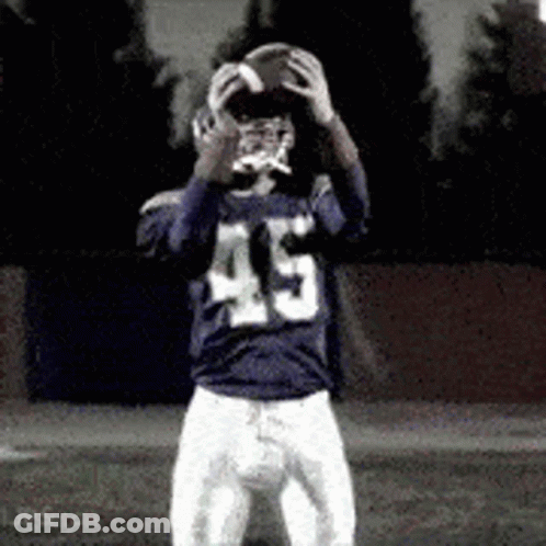 A Football Player With The Number 45 On His Jersey Is Holding A Football In His Hands . GIF