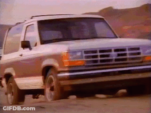 A Ford Bronco Is Driving Down A Dirt Road With Mountains In The Background GIF