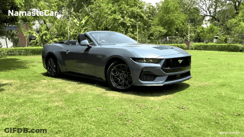 A Ford Mustang Convertible Is Parked In A Grassy Field With Namaste Car Written On The Bottom Right GIF