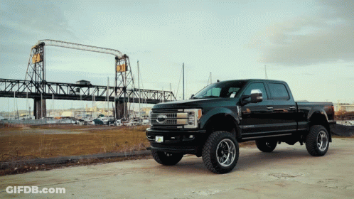 A Ford Truck Is Parked In Front Of A Large Bridge GIF