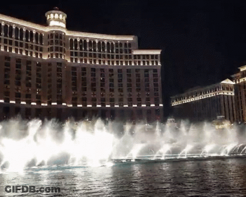 A Fountain In Front Of A Large Building That Is Lit Up At Night GIF