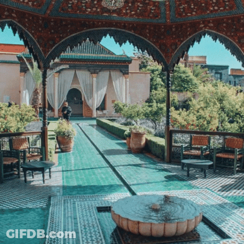 A Fountain Sits In The Middle Of A Courtyard Surrounded By Chairs GIF