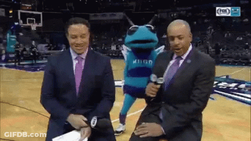 A Frog Mascot Is Being Interviewed By Two Men On A Basketball Court . GIF