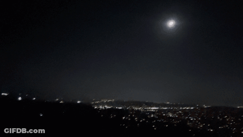 A Full Moon Shines Brightly In The Night Sky Over A City GIF