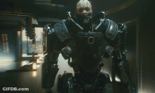 A Futuristic Robot With Red Eyes Is Standing In A Dark Room GIF