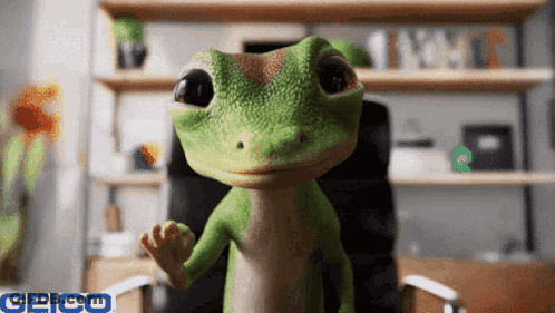 A Geico Lizard Is Sitting In A Chair And Waving At The Camera GIF
