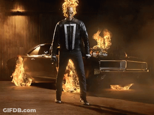 A Ghost Rider Is Standing In Front Of A Car That Is On Fire GIF